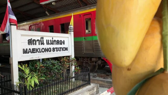 Maeklong Station sign with train parking at local umbrella market (Talad Rom Hub), famous travel destination landmark. Editorial tourism concept - day