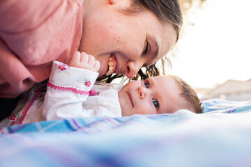 happy young mother playing with her new baby outside on picnic rug