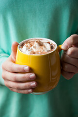 person holding yellow mug brimming with hot chocolate and whipped cream