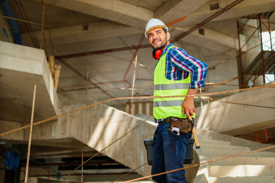A portrait of a foreman in his 40s who descends the stairs with a tool box on the construction site.