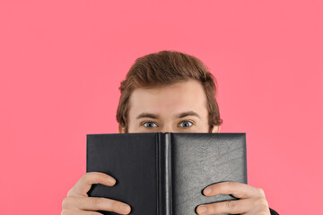 Young amazed man with book on pink background