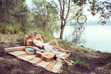 Girl having a picnic by the river with a guitar