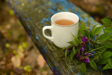 Tea and flowers. Hot tea in a white mug in a spring garden on a bench. Tea cup and floral bouquet on a wooden table soft focus, blurred background