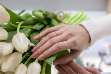 Girl trying on a ring in a jewelry store with white tulips bouquet background. Jewelry and shopping concept. Young woman is choosing ring in the shopping mall. Concept of consumerism, sale, rich life.