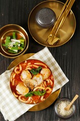 Jjampong Korean Spicy Noodle Soup on Golden Metal Bowl, Served with Green Onion Kimchi.