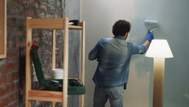 Black man in denim shirt and jeans paints wall in room