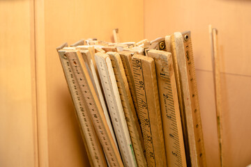 Group of wooden yard sticks and meter sticks with brown background.