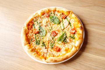 Italian pizza with chicken, cherry tomatoes, mozzarella and parmesan cheese, basil on plate on wooden table. Top view, lifestyle photo.
