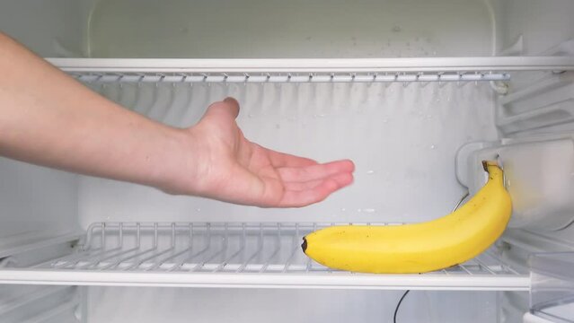The man's hand opens an empty refrigerator and takes one single banana. Conceptual 4k raw video. Idea of ​​economic crisis, food shortage, poverty.