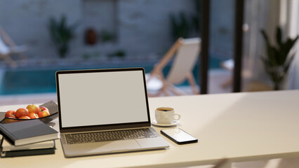 Notebook laptop and copy space on white tabletop house over blurred pool in background.