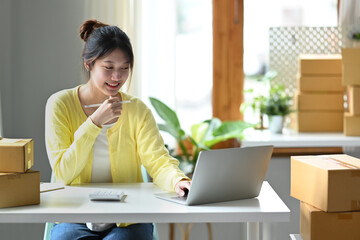 Asian woman business owner confirming orders or checking product purchase order on laptop computer