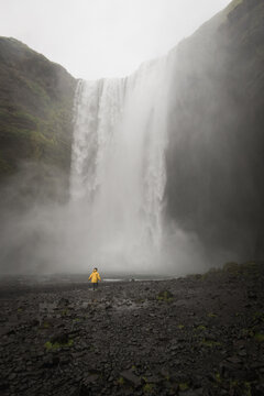 little boy in yellow coat standing near large waterfall Skogafoss in iceland