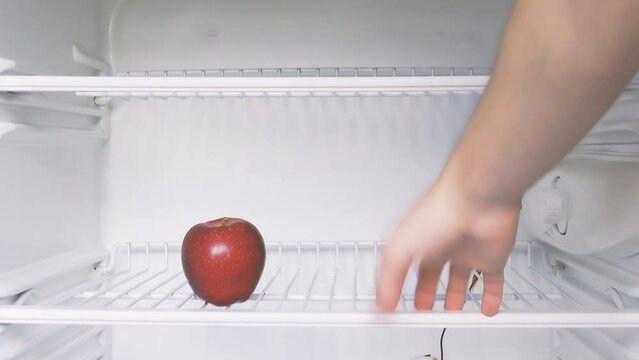 The man's hand opens an empty refrigerator with the word crisis on it and takes one single red apple. Conceptual 4k raw video. Idea of ​​economic crisis, food shortage, poverty.