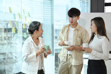 Friendly mature business team leader having discussion with young employees at coffee break in office