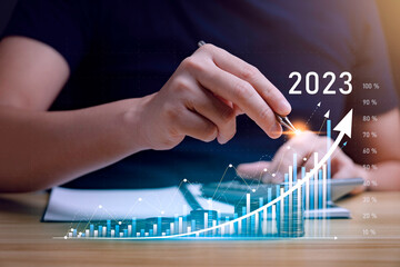 Businessman planning 2023 business growth on desk with virtual hologram chart graph. Calculate income and profit on investments and an increase in the indicators of positive growth