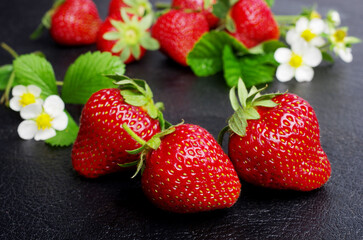 Ripe strawberries with flowers and leaves on a black table.