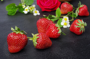 Ripe strawberries with flowers and leaves on a black table.