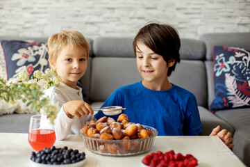 Cute child, boy with pet dog, eating fried doughnuts at home with his siblings