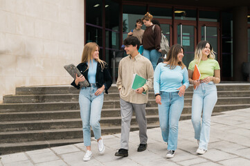 Happy young friends walking near university building after studies