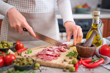 Obraz na płótnie Canvas Woman slicing Spanish sausage fuet salami with knife on a domestic kitchen