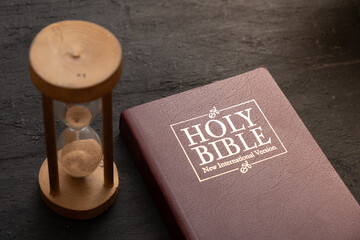 Top view of the Holy Bible on the desktop with hourglass. The concept of Bible study time