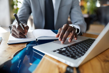 Close-up of unrecognizable businessman in suit sitting at wooden table and using laptop while working on business strategy in cafe