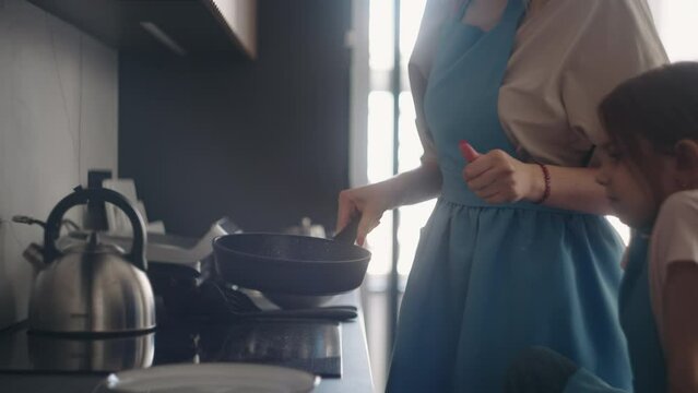 cooking pancakes or omelet in morning, woman and little girl are cooking breakfast, mother is warming oil
