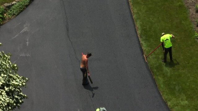 Shirtless Paving Company Employee Smooths Out A Seam In The Asphalt Of A Freshly Paved Driveway. Hard Labor On Hot Summer Day.