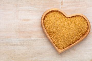 Brown sugar in heart wooden bowl shape on pasttel background.