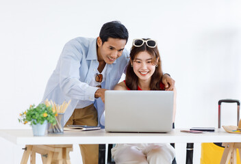Asian young cheerful lovely handsome husband and beautiful wife couple sitting standing smiling together at desk in living room while female using laptop notebook computer working online from home