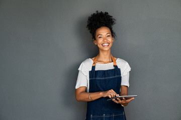 Black happy waitress in apron using digital tablet to take orders - obrazy, fototapety, plakaty