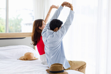 Asian unrecognizable unknown male female husband and wife traveler lover couple in casual outfit sitting stretching arms up while arriving at hotel bedroom resting relaxing in summer vacation weekend