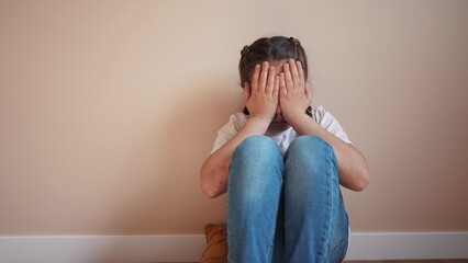 sad girl sitting in the corner crying a covered her face with her hands. family violence abuse...