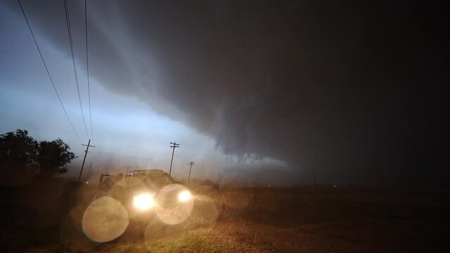 Dangerous thunderstorm moving in at night as it rains and wind blows looking at car with headlights on.