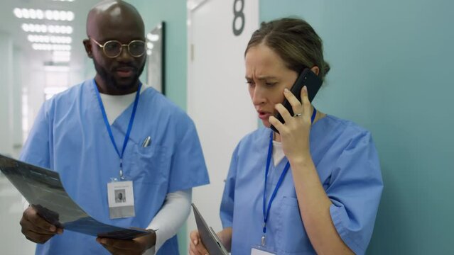 Stressed nurse standing in hospital corridor talking on the phone