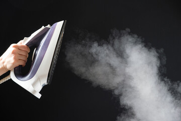 An iron with a steam generator sprays white hot steam on a black background. Steaming clothes,...