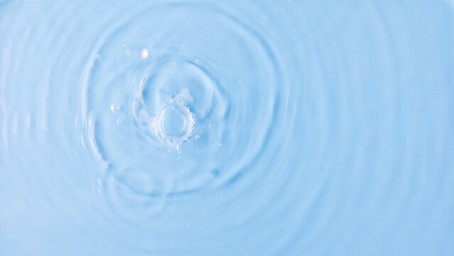 Drops fall down into clear fresh water on light blue background view from above