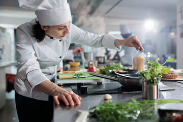 Culinary expert putting fresh chopped herbs in pan while cooking gourmet dish for dinner service at fine dining restaurant. Head chef preparing organic meal in professional kitchen. - Powered by Adobe