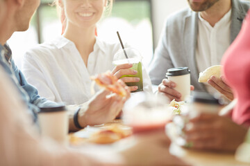 Close-up of smiling young friends in casual outfits sitting at table and drinking non-alcoholic beverages and eating unhealthy food