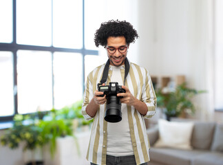 photography, profession and people and concept - happy smiling man or photographer in glasses with digital camera over home room background