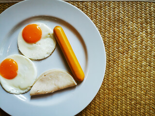 Fried eggs, sausages, ham in a white plate