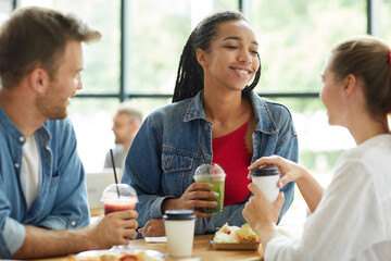 Smiling attractive young Black woman in denim jacket standing at table and enjoying time with friends