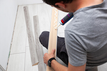 A worker applies glue to a baseboard before installing it on the floor