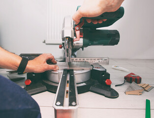 A worker cuts a skirting board made of fibreboard with a miter saw