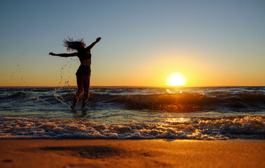 The girl swims in the sea, splashes in the water at sunset. Relaxation and happy pastime. Summer vacations.