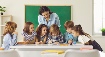 Young caucasian teacher and children group looking at classmate doing homework writing on copybook....