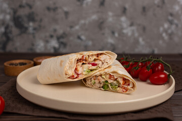Shawarma with chicken and vegetables, grilled, cut into two parts, on a plate with cherry tomatoes
