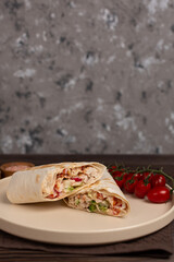 Shawarma with chicken and vegetables, grilled, cut into two parts, on a plate with cherry tomatoes, open space