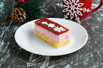 Delicious strawberry mousse cake with winter decor snowflakes on a white plate, New Year's decor and a red cup with tea on a gray background.