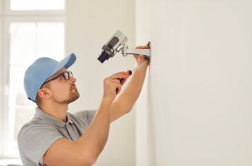 Professional male surveillance camera installer mounts it on wall inside new home or office. Side...